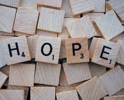 Auf dem Kopf liegende Scrable-Steine. Obenauf vier Steine mit den Buchstaben nach oben. Sie geben das Wort "Hope"
