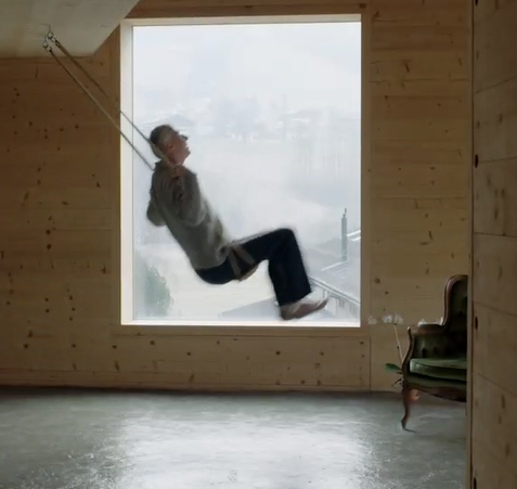 Ein Mann, der in einem holzvertäfelten Raum vor einem großen Fenster schaukelt.